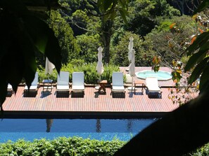 A pool area with lounge chairs and umbrellas, surrounded by greenery. - Pousada do Cedro (Santo Antônio do Pinhal)