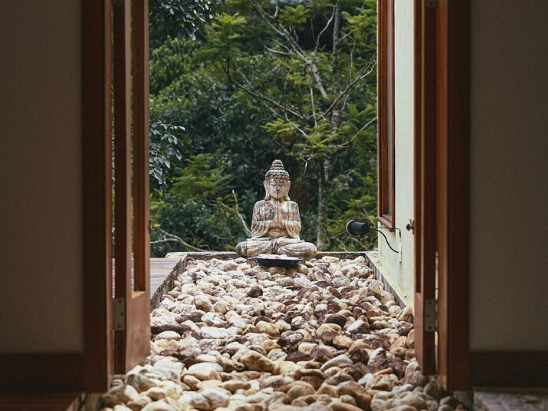 Una habitación con un amplio ventanal, una estatua sobre un pedestal, y un camino de piedra que conduce al ventanal.