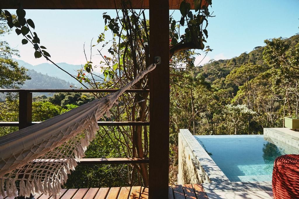 Uma rede sobre um deck de madeira com vista para uma piscina cristalina e vegetação exuberante.