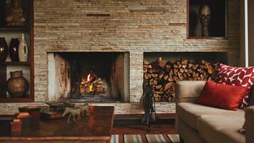 Una sala de estar con chimenea de piedra, un sofá con cojín rojo y un repisa de la chimenea con adornos.