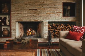 A living room with a stone fireplace, a sofa with a red cushion, and a fireplace mantel with decorative items. - Pousada do Cedro (Santo Antônio do Pinhal)