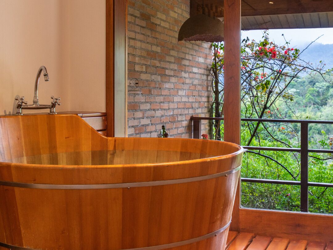 A wooden bathtub in a room with a brick wall and a view of greenery.