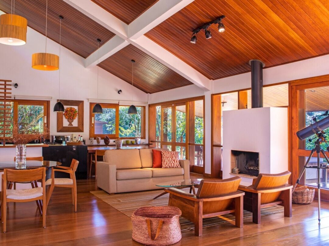 Amplia sala de estar con chimenea, techo de madera y ventanas grandes.