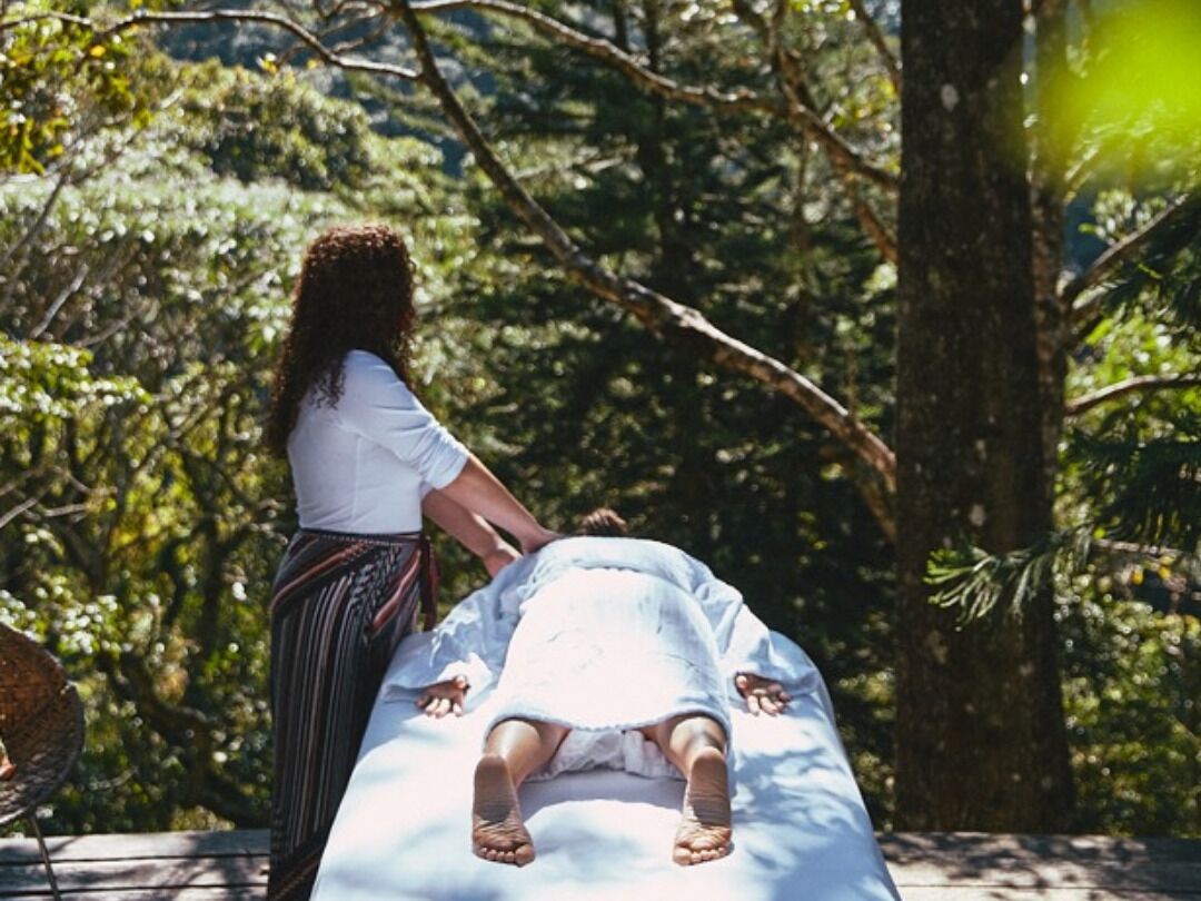 Una persona recostada en una camilla de masaje al aire libre, rodeada de árboles.