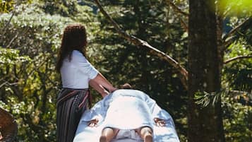 Una persona recostada en una camilla de masaje al aire libre, rodeada de árboles.