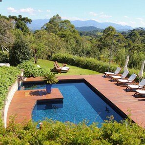 A swimming pool with a wooden deck, lounge chairs, and a potted plant. - Pousada do Cedro (Santo Antônio do Pinhal)