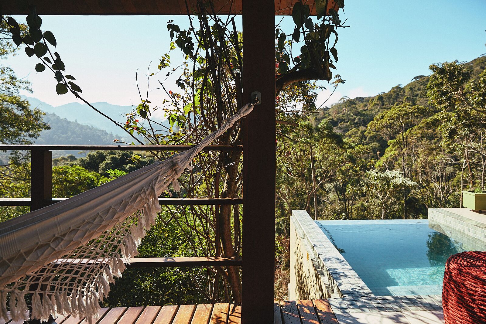 Uma rede em um deck de madeira com vista para uma piscina e montanhas ao fundo.