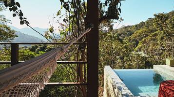Uma rede em um deck de madeira com vista para uma piscina e montanhas ao fundo.