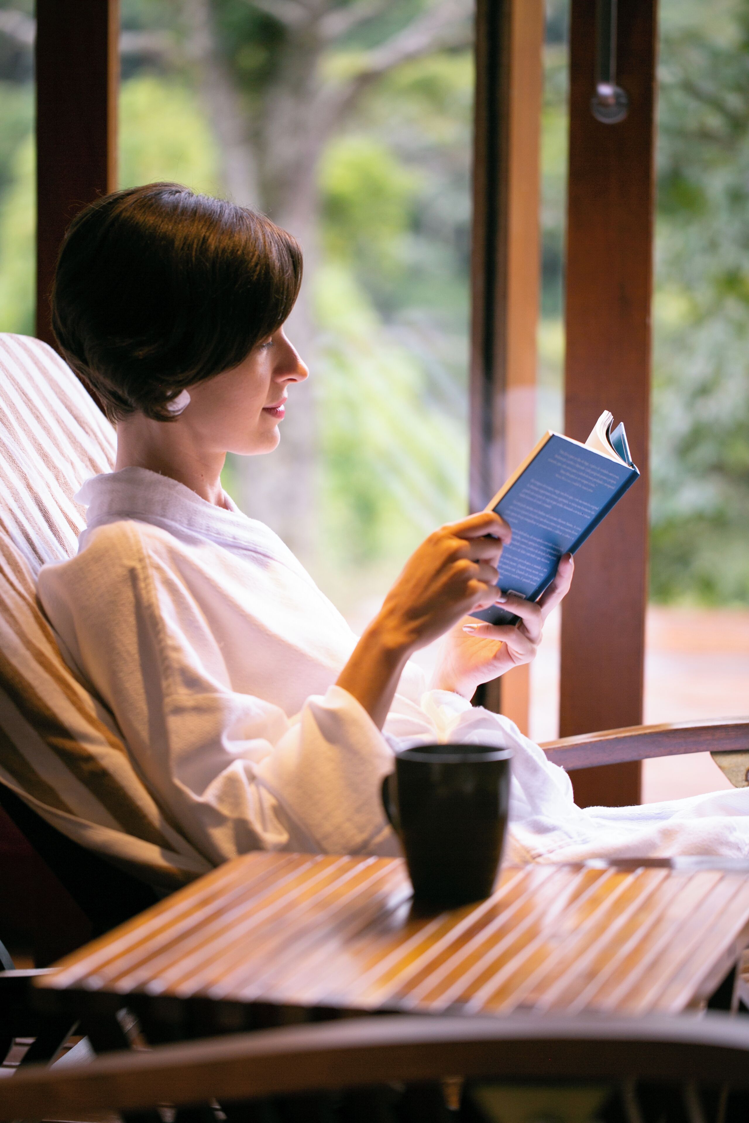Una persona recostada en una silla con un libro y una taza, evocando un momento de lectura o descanso.