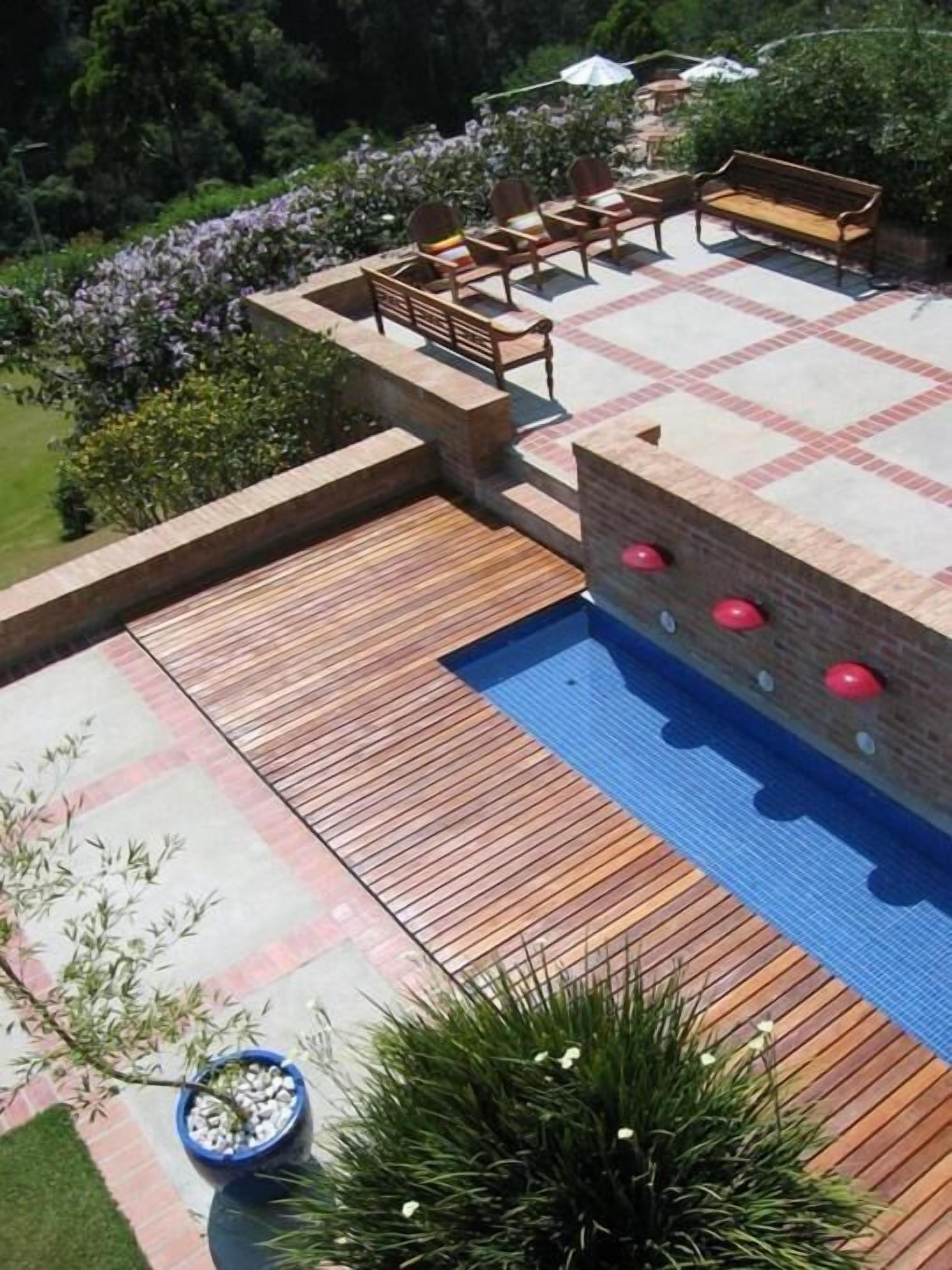 Una zona de piscina con terraza de madera, mobiliario y un muro de ladrillo.
