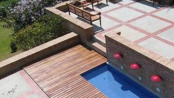 Una zona de piscina con terraza de madera, mobiliario y un muro de ladrillo.