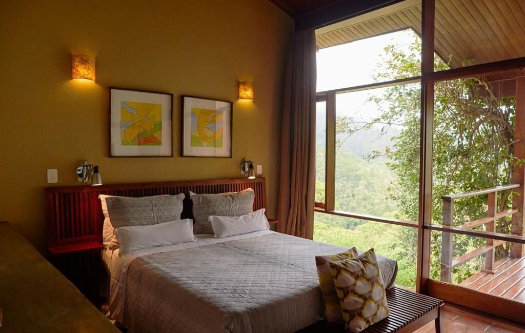 Une chambre à coucher avec un grand lit, deux lampes fixées au mur et une fenêtre donnant sur un paysage verdoyant.