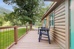 Une cabane en bois dotée d’une terrasse, d’une rambarde en métal et offrant une vue sur un paysage verdoyant.