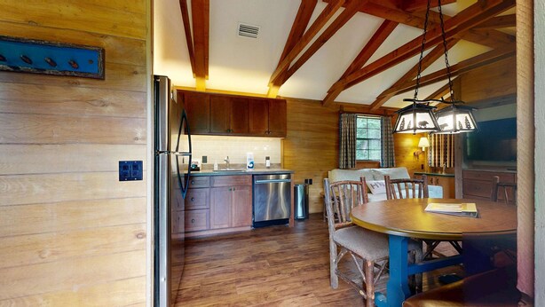 A rustic kitchen with wooden beams, a dining area with a wooden table and chairs, and a built-in dishwasher. - Riverfront Wilderness Cabin (Cullowhee)