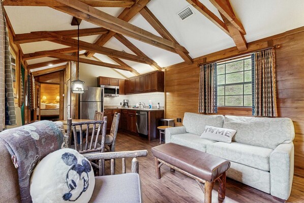 A rustic cabin interior with exposed wooden beams, a kitchenette, a sofa, and a dining area.