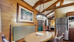 A wooden interior with a round dining table, chairs, a hanging light fixture, and a refrigerator. - Riverfront Wilderness Cabin (Cullowhee)