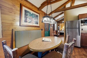 A wooden interior with a round dining table, chairs, a hanging light fixture, and a refrigerator. - Riverfront Wilderness Cabin (Cullowhee)