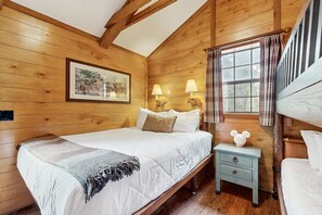 A wooden room with a bed, a nightstand, a lamp, a picture on the wall, and a window with curtains.