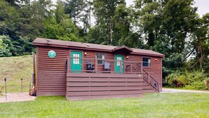 A rustic cabin with a green door, a small porch, and a staircase leading to the entrance. - Riverfront Wilderness Cabin (Cullowhee)
