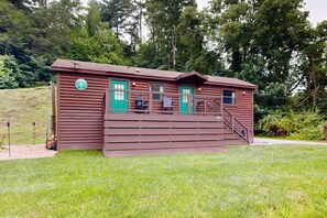 A rustic cabin with a green door, a small porch, and a staircase leading to the entrance. - Riverfront Wilderness Cabin (Cullowhee)