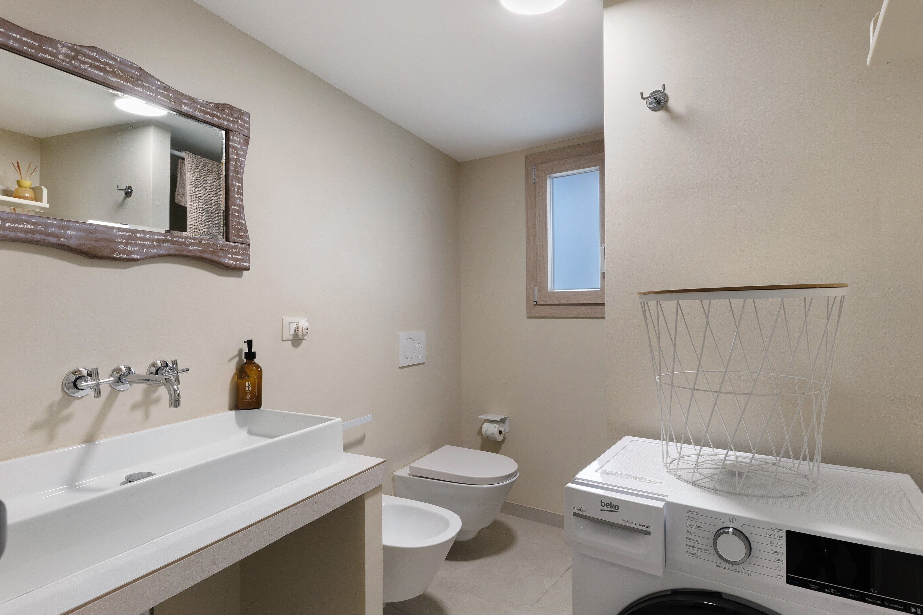 Een moderne badkamer met een witte wastafel, een spiegel, een toilet en een wasmachine.