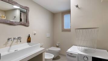 Een moderne badkamer met een witte wastafel, een spiegel, een toilet en een wasmachine.