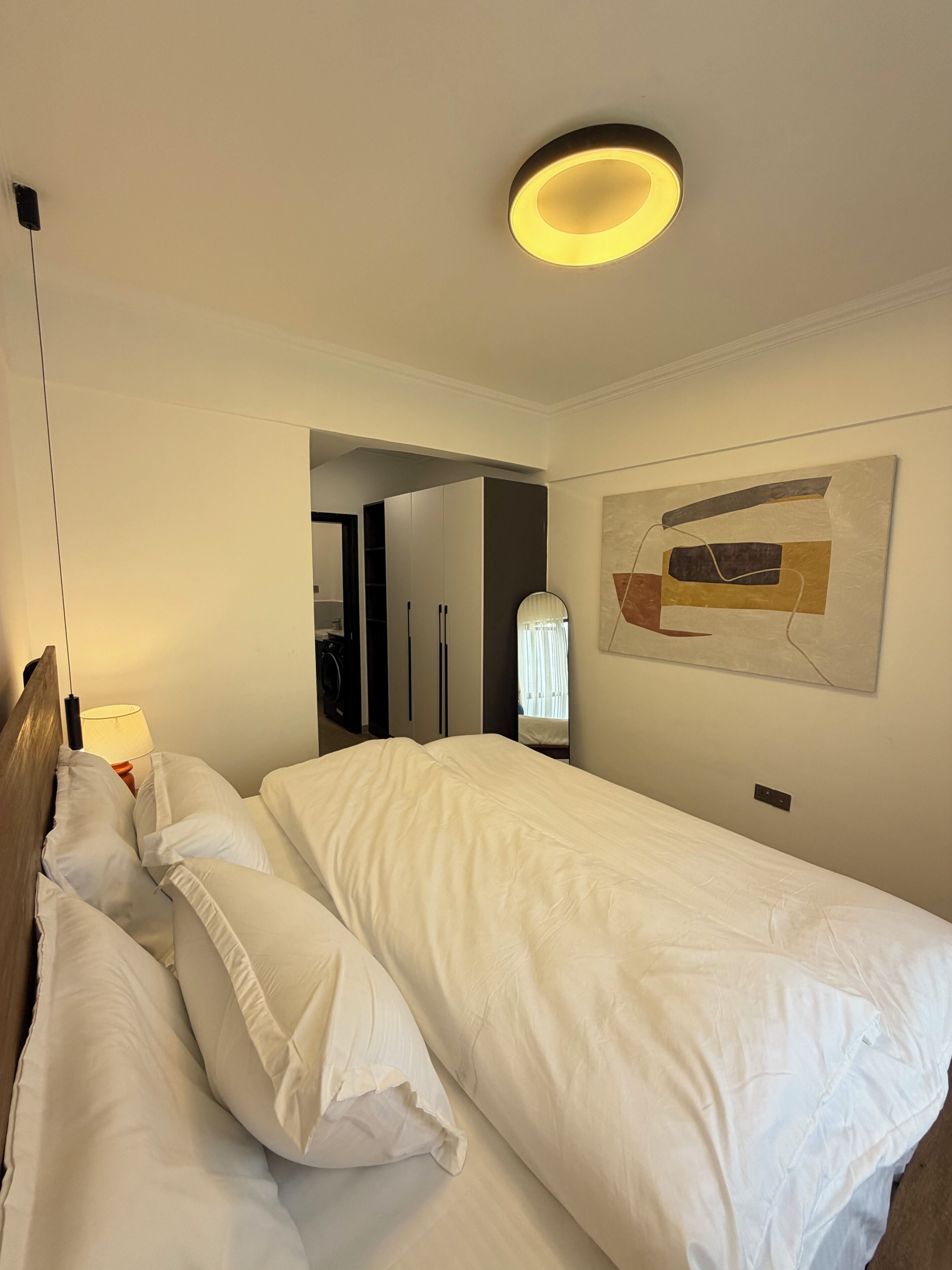 Et hotelværelse med en seng, et spejl, et maleri og en loftlampe.