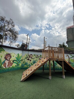 A children's play area with a slide and climbing structure, surrounded by a mural of jungle animals. - Luxury King Suite | Balcony, Rooftop Pool, Gym (Nairobi)
