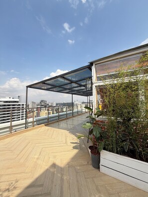 A rooftop terrace with a wooden floor, a glass enclosure, and potted plants. - Luxury King Suite | Balcony, Rooftop Pool, Gym (Nairobi)