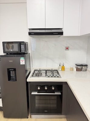 A kitchen with a water dispenser, a microwave, a stove, and cabinets. - Luxury King Suite | Balcony, Rooftop Pool, Gym (Nairobi)