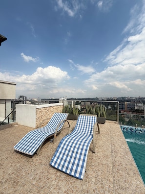 A rooftop terrace with two lounge chairs, a swimming pool, and a city view. - Luxury King Suite | Balcony, Rooftop Pool, Gym (Nairobi)