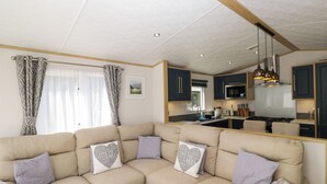 A modern living room with a beige sectional sofa, a kitchen with dark cabinets, and a dining area. - High Perch (Windermere)