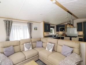 Una sala de estar moderna con un sofá seccional color beige, una cocina con armarios oscuros y un comedor.