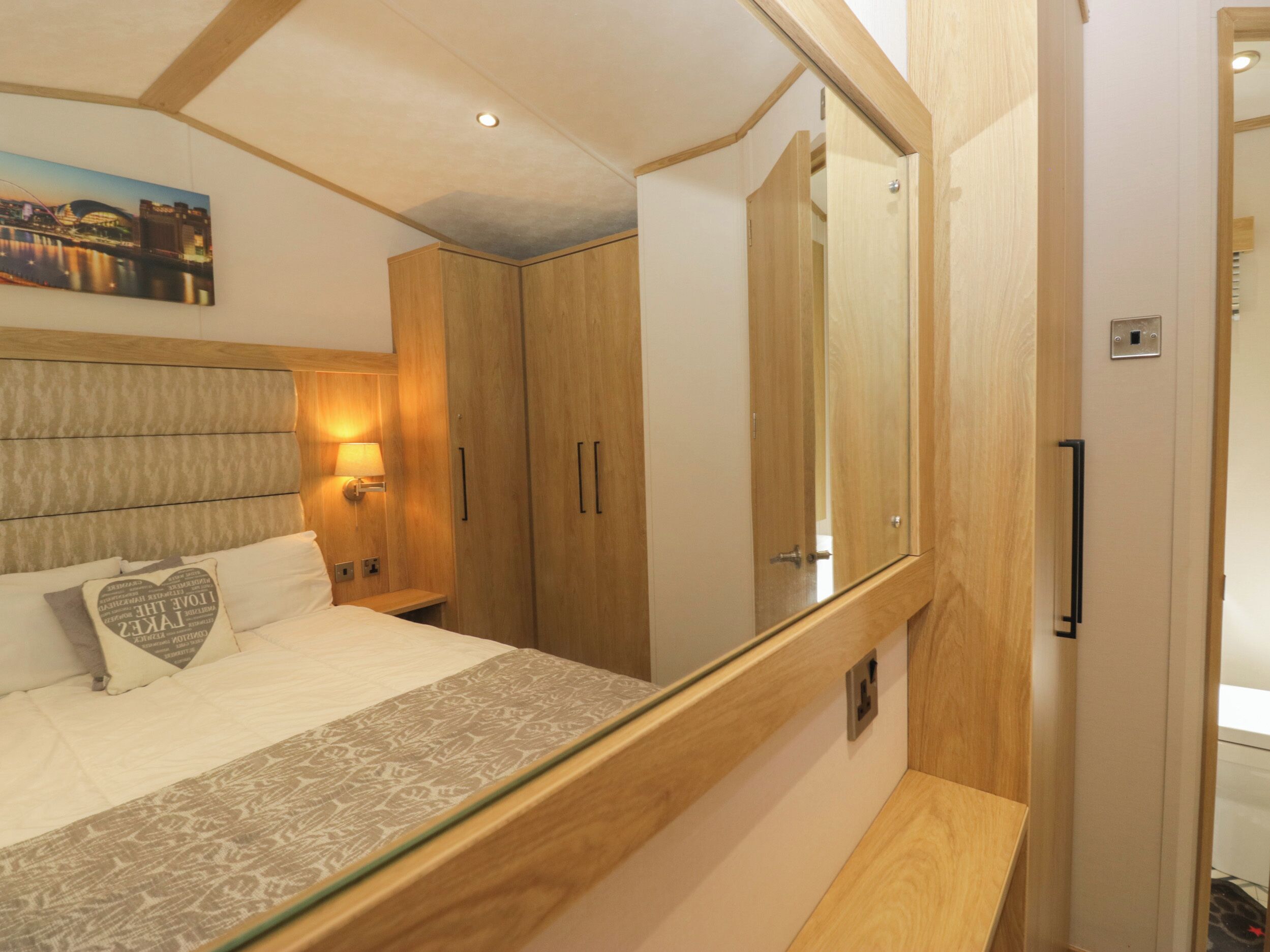 A hotel room with a bed, a nightstand, a mirror, and wooden wardrobes.