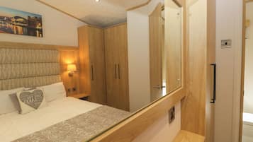 A hotel room with a bed, a nightstand, a mirror, and wooden wardrobes.