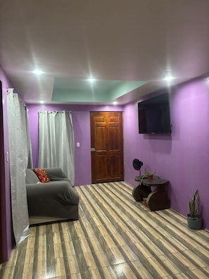 A room with a bed, a television mounted on the wall, a wooden door, and a small round table with a plant. - Vrbo Property (Provincia de Guanacaste)