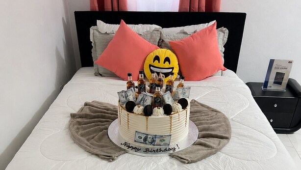 Uma cama com bolo de aniversário, almofadas e mesa de cabeceira com um celular.