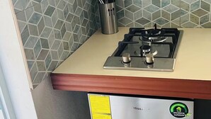 Cozinha compacta com fogão a gás, suporte de utensílios em aço inoxidável e painel de azulejos.