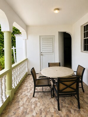 A covered patio area with a round table and four chairs, a white door, and a window with a view of greenery. - Vibra Lux Island Escape Cozy 1BR Near Beaches & Philipsburg (Philipsburg)