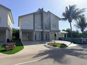 A modern multi-story residential building with a flat roof, balconies, and a well-maintained lawn with red flowers. - #3 2-bedroom condo in tranquil Savannah with cool AC breeze (Savannah)