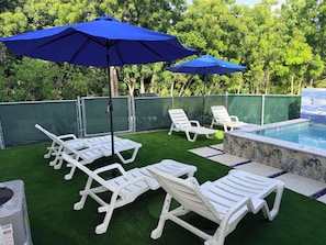 A poolside area with artificial grass, white lounge chairs, and blue umbrellas. - #3 2-bedroom condo in tranquil Savannah with cool AC breeze (Savannah)