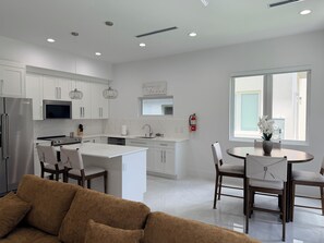 A modern kitchen with white cabinetry, a central island, and a dining area with a round table and chairs. - #3 2-bedroom condo in tranquil Savannah with cool AC breeze (Savannah)