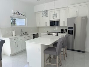 A modern kitchen with white cabinetry, stainless steel appliances, and a central island with bar stools. - #4 Delightful 2-bedroom condo with AC in charming Savannah (Savannah)