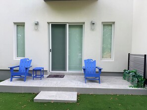 A patio with two blue chairs and a small table, a sliding glass door, and a concrete step leading to a grassy area. - #4 Delightful 2-bedroom condo with AC in charming Savannah (Savannah)