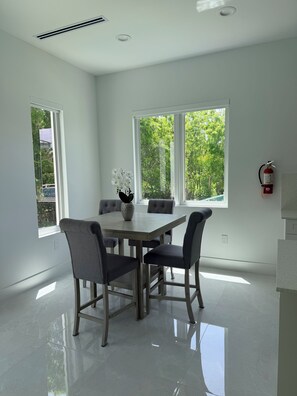 Une salle à manger moderne avec une table et des chaises, de grandes fenêtres et un extincteur fixé au mur.
