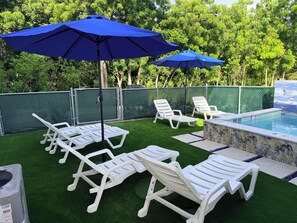 A poolside area with artificial grass, white lounge chairs, and blue umbrellas. - #4 Delightful 2-bedroom condo with AC in charming Savannah (Savannah)