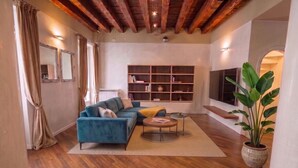 A modern living room with a blue sofa, wooden flooring, a bookshelf, and a large plant. - ApartmentsArena - Capitolium Verona 5 (Verona)