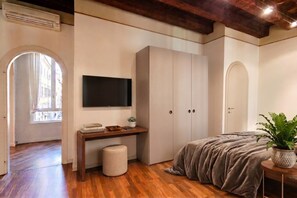 Une chambre avec un plancher en bois, un lit recouvert d’une couverture grise, un téléviseur fixé au mur et une armoire.