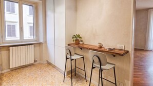 A compact kitchen with a wooden countertop, two bar stools, a radiator, and a window with shutters. - ApartmentsArena - Capitolium Verona 5 (Verona)