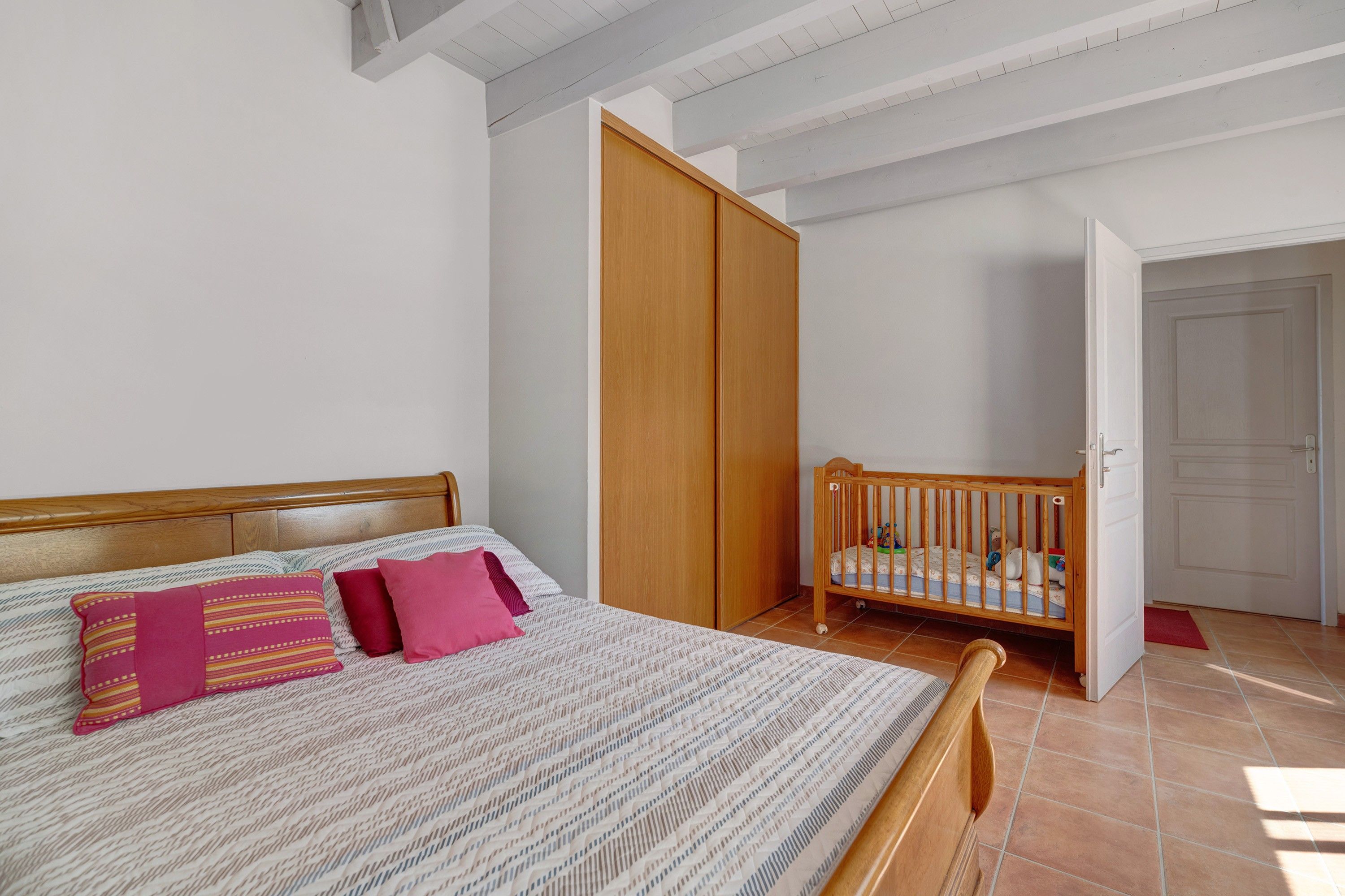 Une chambre à coucher avec un lit, un berceau en bois, une armoire et une porte.